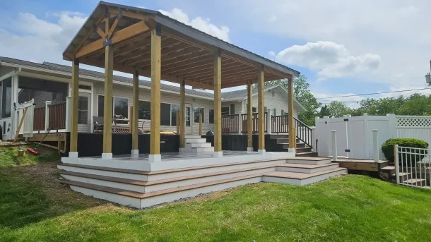 A newly built deck with a pergola and stairs, featuring clean, modern steps leading up to a raised platform. The deck is surrounded by green grass and a white privacy fence, offering a cozy and stylish outdoor space.